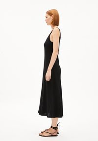 Black ribbed maxi dress with a fitted bodice, sleeveless design, and flared hem. Paired with black strappy sandals for an overall sleek look.