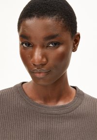 Grauer gerippter Pullover mit rundem Ausschnitt. Nahaufnahme des Gesichts eines Modells mit glatter Haut und dunklem, kurzem Haar. Weißer Hintergrund.