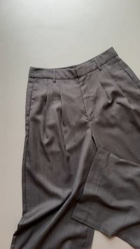 Harmaat, poimutetut housut, jotka on valmistettu sileästä kankaasta. Niissä on sovitettu malli ja siistit linjat, sivutasku ja hienovarainen kiilto.