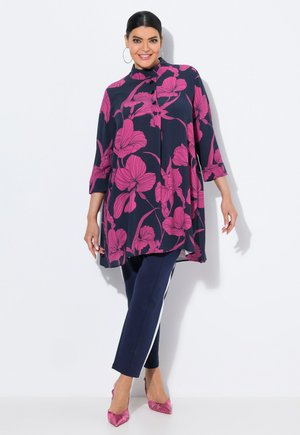 Marineblaue Bluse mit pinkem Blumenmuster, 3/4-Ärmel, Knopfdetails vorne, kombiniert mit marineblauen Hosen mit weißen Seitenstreifen und pinken Absätzen.