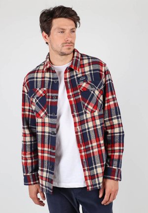 Chemise flanelle à carreaux en bleu marine, rouge et crème ; dotée de deux poches poitrine et d'une fermeture à boutons ; texture douce et coupe structurée.