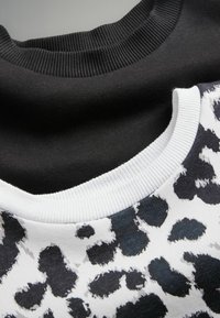 Due felpe: una nera con colletto a costine, l'altra con una base bianca caratterizzata da una stampa leopardata nera, anch'essa con colletto a costine.