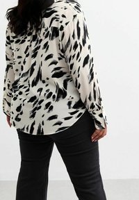 Lange mouwen blouse van lichtgewicht stof, met een zwart-wit abstract patroon, een gebogen zoom en knoopmanchetten. Gepaard met zwarte broek.