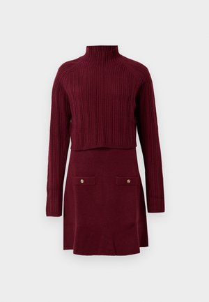 Burgundy knitted dress with a high ribbed neck, long sleeves, and a fitted skirt featuring two buttoned pockets at the front.