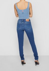 Džínový top s kulatým výstřihem a tvarovaným pasem, v kombinaci s modrými džínami s vysokým pasem. Výrazný zadní design a štítek na džínách. Černé podpatky.
