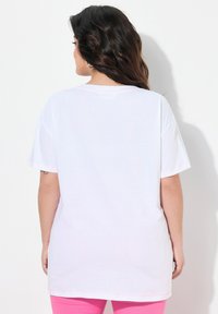 Weißes, übergroßes T-Shirt mit kurzen Ärmeln, runder Ausschnitt und pinken Nähten an den Säumen. Glatte Stoffoberfläche.