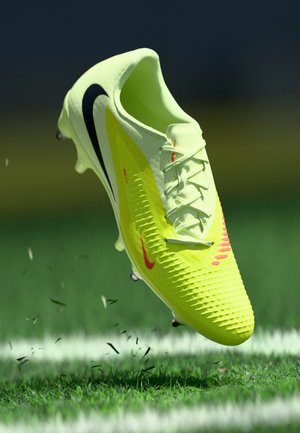 Scarpa da calcio gialla con design testurizzato, accenti neri e rossi, lacci e tacchetti prominenti, esposta su erba verde e linee bianche.
