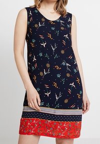 Mörkblå ärmlös klänning med blomstertryck, röd fåll och mönstrad kant. Tillverkad i lätt tyg, med rund halsringning.