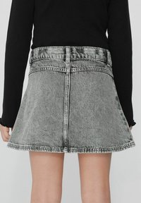 Jupe en denim gris avec une forme évasée, ourlet brut et couture visible. Portée taille haute, avec une poche arrière et un design simple.