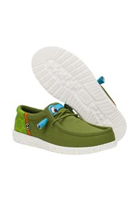 Grüne Leinenschuhe mit abgerundetem Zeh, blauen Akzenten und einem Schildkrötenmotiv an der Seite. Weiße Gummisohle mit einem gesprenkelten Muster.