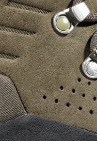 Męskie buty do wędrówki z oliwkowozielonego zamszu, czarną gumową podeszwą, perforowanymi detalami oraz metalowymi akcentami przy systemie sznurowania.