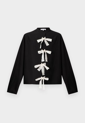 Crna bluza s dugim rukavima s četiri bijele mašne od čipke s rupicama niz prednji dio i malim stojećim ovratnikom.