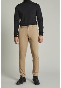 Czarny sweter z golfem w prążki, zestawiony z jasnobeżowymi spodniami garniturowymi, z zapięciem na guziki i czarnymi butami eleganckimi.