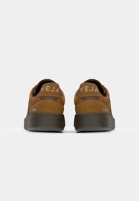 Brown suede sneakers with durable gray rubber soles. Features include "VEJA" branding and subtle heel accents. Clean, modern design.