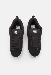 Black sneakers with a smooth textile upper, laces, padded collar, and a white rubber sole. Features a logo on the tongue and side.