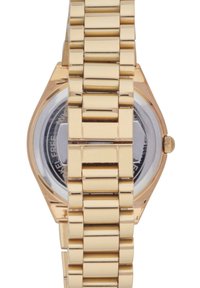 Montre en métal doré avec un boîtier octogonal, un bracelet à maillons, et un cadran noir et blanc visible à travers un fond transparent.