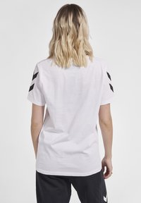 Hvid kortærmet t-shirt lavet af bomuld, med sorte chevron-mønstre på ærmerne, i en afslappet pasform og blød tekstur.