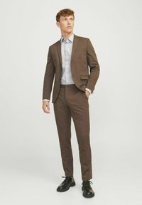 Bruin pak met een slim fit, blazer met één knop, bijpassende broek en een licht gestreept overhemd. Zwarte veterschoenen maken de look compleet.