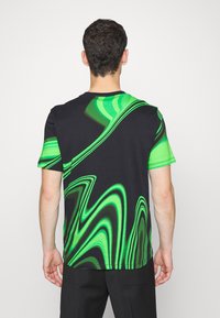 Camiseta negra con un patrón de olas abstractas en verde. Mangas cortas y cuello redondo. Tejido suave con una textura lisa.