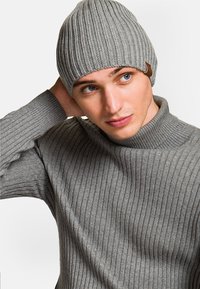 Szara, prążkowana czapka beanie o stożkowym kształcie i małej skórzanej metce. Noszona z dopasowanym, szarym, prążkowanym swetrem. Gładka faktura.