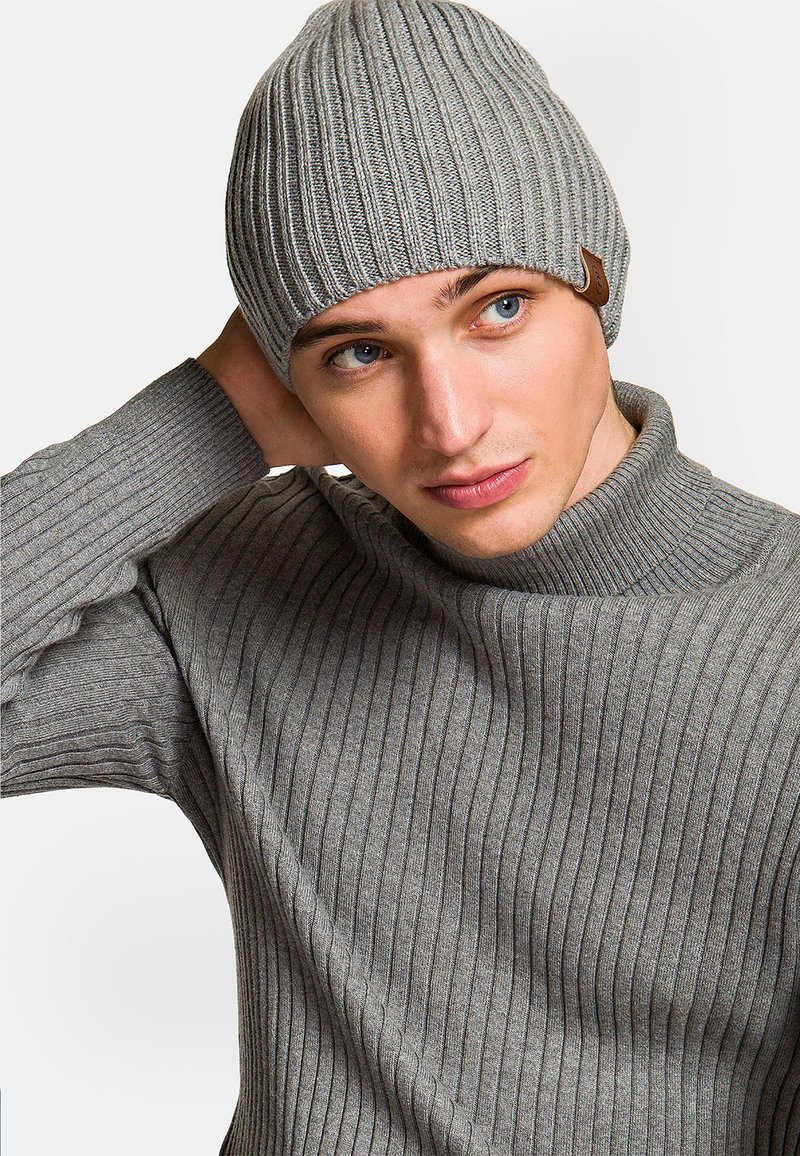 Szara, prążkowana czapka beanie o stożkowym kształcie i małej skórzanej metce. Noszona z dopasowanym, szarym, prążkowanym swetrem. Gładka faktura.