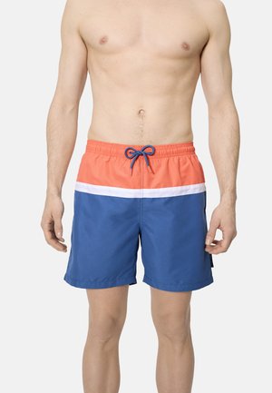 Hombre con pantalones cortos de baño azules con cinturilla coral, raya blanca y cordón azul, de pie con los brazos relajados a los lados.