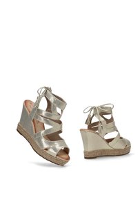 Sandalias cuña metálicas doradas con punta abierta, tiras entrelazadas y detalles de borlas. Plataforma envuelta en yute para añadir textura.