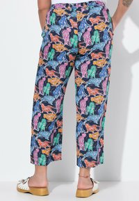 Farverige, mønstrede bukser med en marineblå baggrund og forskellige leoparder i orange, pink, grøn, blå og sort. Korte i længden.