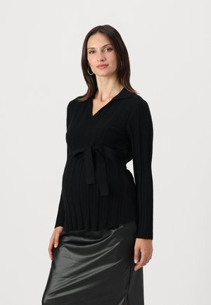Black ribbed maternity sweater with a V-neck, long sleeves, and a waist tie. Paired with a glossy black skirt featuring a side slit.