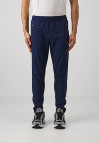 Marine sportbroeken met elastische tailleband, ritszakken aan de zijkanten en taps toelopende benen. Draag ze met grijze en zwarte hardloopschoenen.