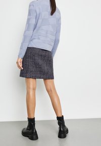 Lyseblå, struktureret sweater med geometriske mønstre, parret med en mørk tweed mini-skirt og sorte, chunky ankelstøvler.