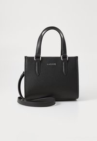 Sac à main en cuir noir texturé avec des poignées courtes et une bandoulière amovible. Doté d'un logo "LACOSTE" en argent à l'avant.