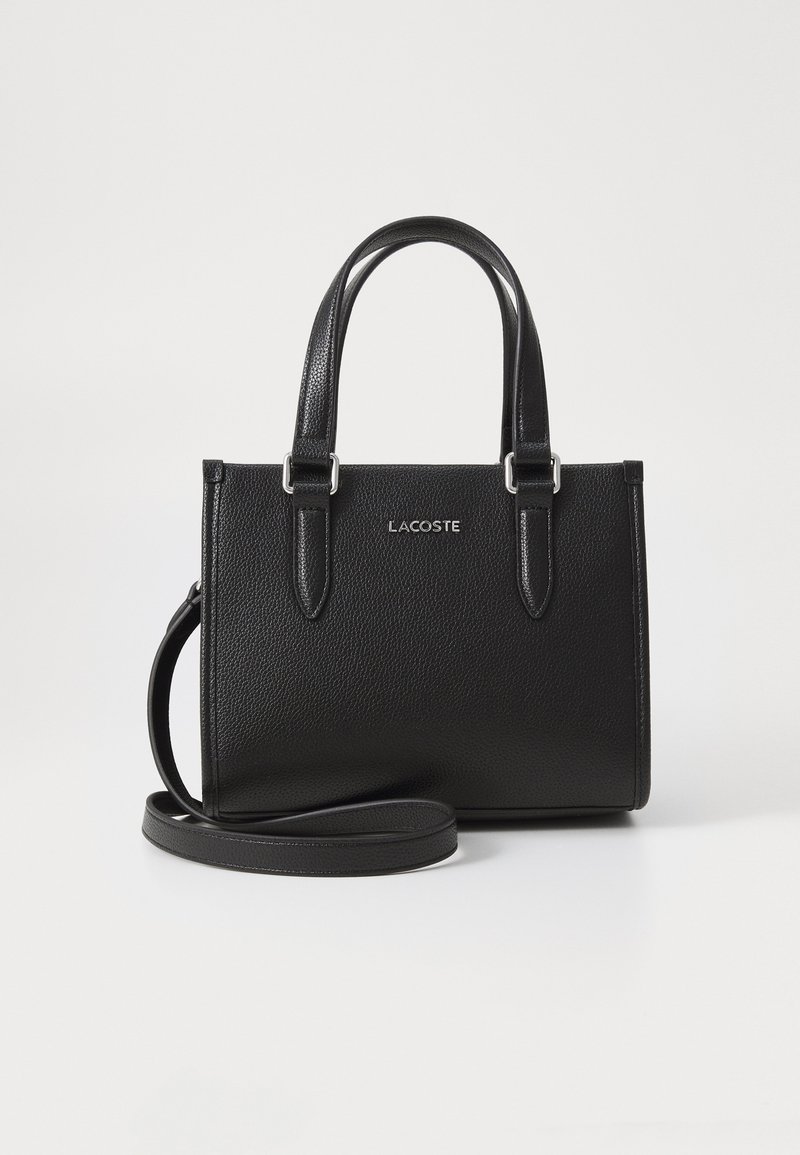 Sac à main en cuir noir texturé avec des poignées courtes et une bandoulière amovible. Doté d'un logo "LACOSTE" en argent à l'avant.