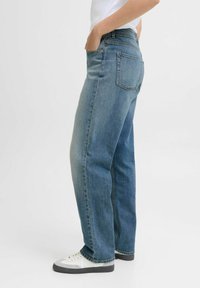 Jeans de mezclilla azul claro con un corte relajado, cinco bolsillos y un diseño de pierna recta. Llevados con zapatillas blancas y grises.