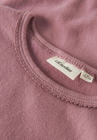 Primo piano di un colletto di un capo lavorato a maglia rosa con etichetta del marchio Lil’ Atelier e cartellino delle taglie 7-8 anni, 122-128 cm.