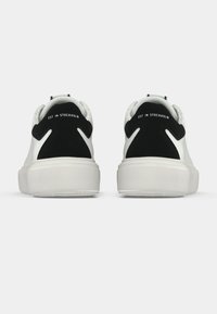 Λευκά αθλητικά παπούτσια με υφή στη σόλα και μαύρες σουέντ λεπτομέρειες στη φτέρνα, με την επιγραφή "EST. IN STOCKHOLM" στο πίσω μέρος.