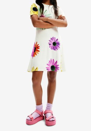 Biała sukienka z krótkim rękawem w kolorowe wzory kwiatowe. W połączeniu z różowymi sandałami na platformie i jasnofioletowymi skarpetkami.
