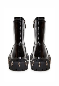 Musta lakattu nahkaa oleva nilkkabootsit, joissa on tukeva pohja ja metalliset niitit, vetoketjusuljenta ja teksturoitu sivupinnoite.