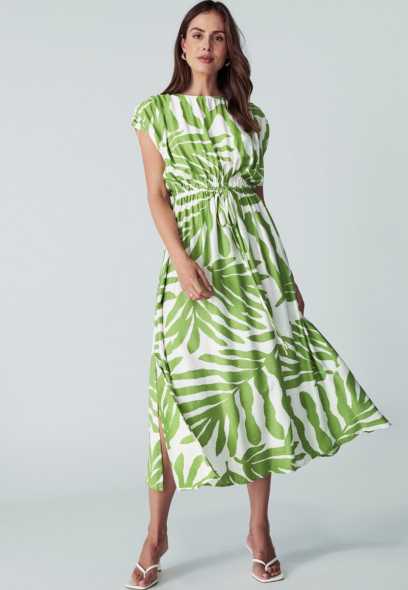 Haljina s uzorkom palminih listova u zelenoj i bijeloj boji, skupljena u struku, s kapicama i lepršavom suknjom koja ima bočne proreze.