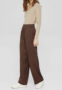 Pantaloni in satin marroni a gamba larga con vita elastica abbinati a un top beige a maniche lunghe con rifiniture in pizzo sul collo.