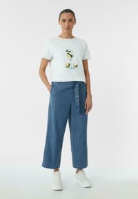 Witte t-shirt met korte mouwen met een grafisch ontwerp van een cocktail met citrusvruchten. Gecombineerd met loszittende denim broek en witte sneakers.