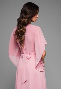 Fodrad rosa klänning med flödande, genomskinliga kimonoärmar. Knuten i midjan med en sløjfa, med en mjuk, lätt textur.