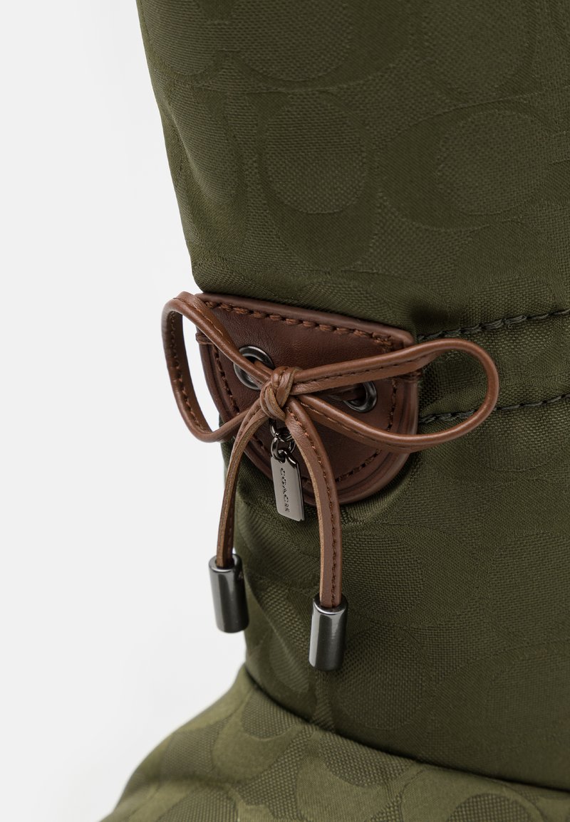 Zielona tkanina w wzory z teksturowym wykończeniem, z brązowym zapięciem na suwak wykonanym ze skórki oraz metalowymi akcentami u góry.