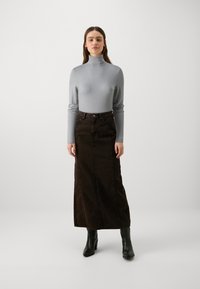 Un haut col roulé gris associé à une longue jupe en denim marron foncé. L'ensemble comprend des bottes à talons noires. La texture semble lisse avec une coupe ajustée.