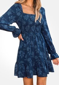 Vestido azul marino con mangas largas abullonadas, escote cuadrado, corpiño fruncido, textura floral y detalles de dobladillo con volantes.