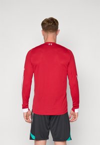 Rød langærmet træningsskjorte med en tekstureret overflade og hvide detaljer på ærmerne. Crew neck design, parret med sorte shorts.