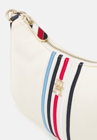 Crèmekleurige handtas met verticale blauw, marineblauw, rood en wit gestreepte patronen, gouden merkembleem en gouden rits met rood, wit en marineblauwe strepen.