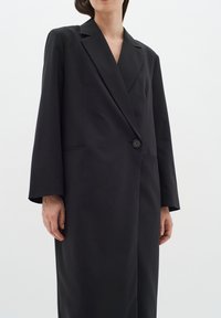 Juodas švarkas, pagamintas iš lygaus audinio, turi aštrų apykaklę, ilgomis rankovėmis, vieną mygtuko užsegimą ir dvi šonines kišenes.