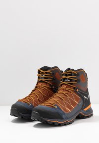 Bottes de randonnée avec partie supérieure en mesh orange, semelle en caoutchouc noir, embout renforcé et système de laçage rapide pour un ajustement sécuritaire et une durabilité accrue.