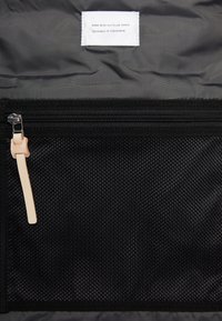 Wnętrze czarnego plecaka z siateczkową kieszonką na zamek, kremowym uchwytem suwaka oraz etykietą z napisem "Wykonano z przetworzonego materiału". Teksturowany materiał.